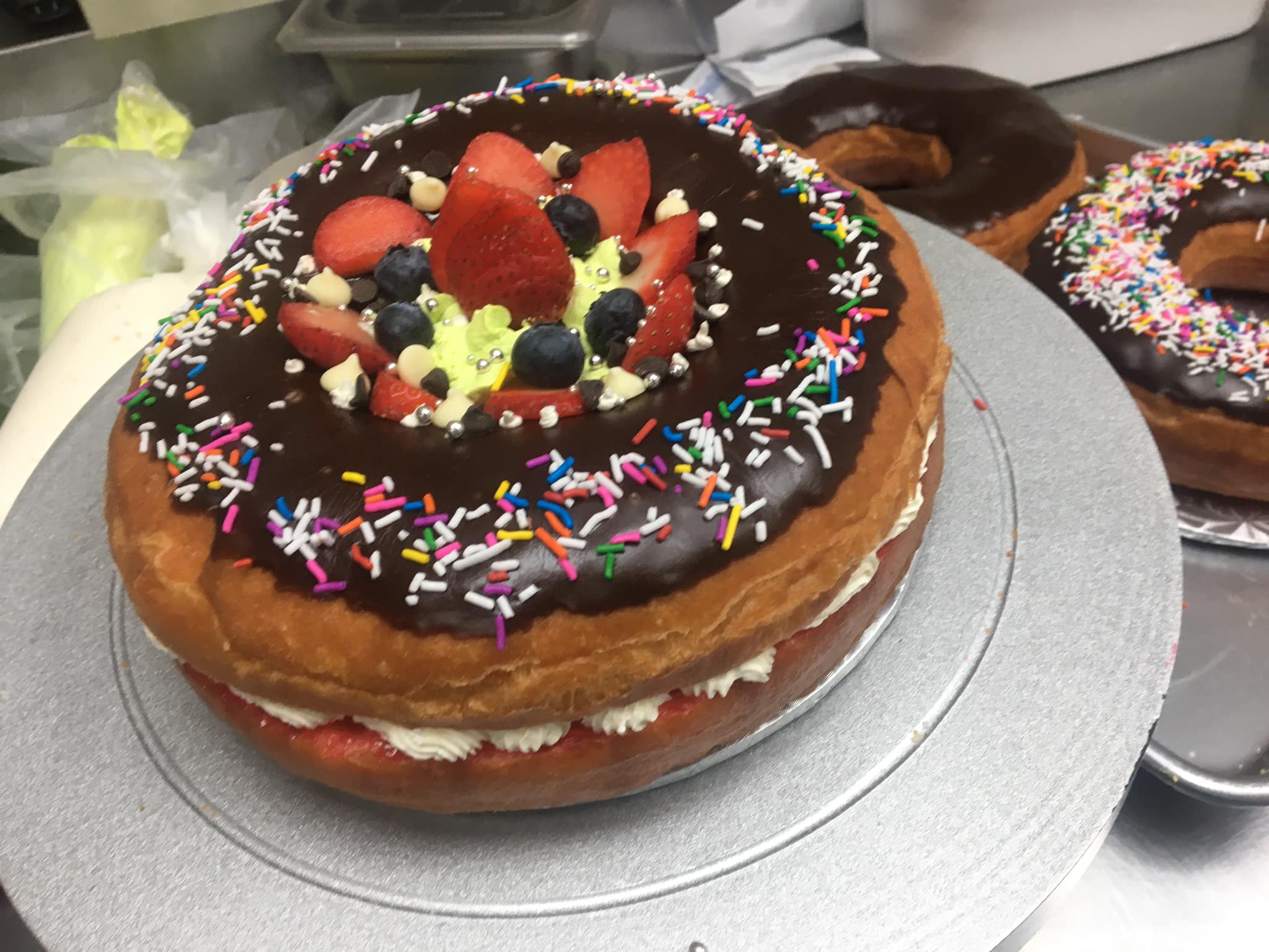 Large chocolate donut cake decorated with strawberries, blueberries, and rainbow sprinkles