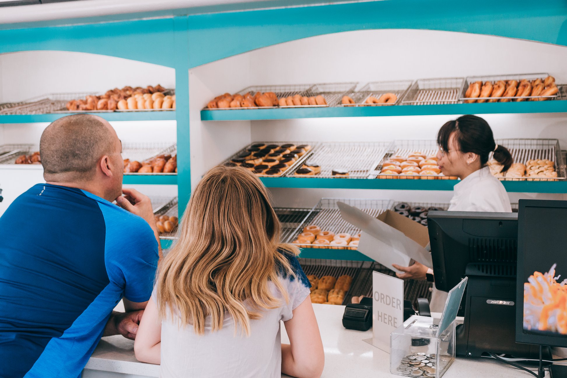 Customers ordering at the GrandDonut counter with fresh donut shelves and teal interior