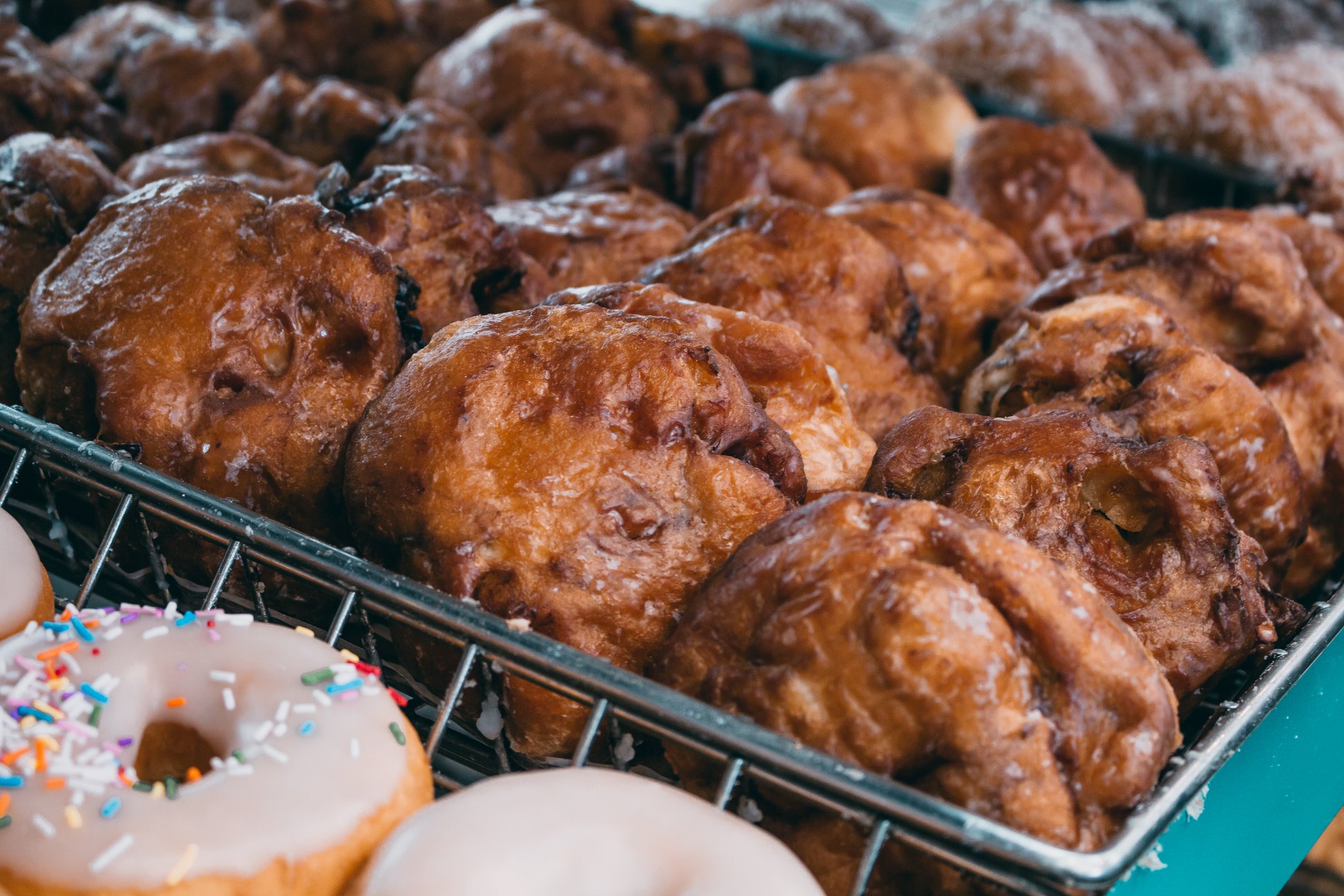 Close-up of fresh apple fritters glistening with glaze on teal bakery shelves