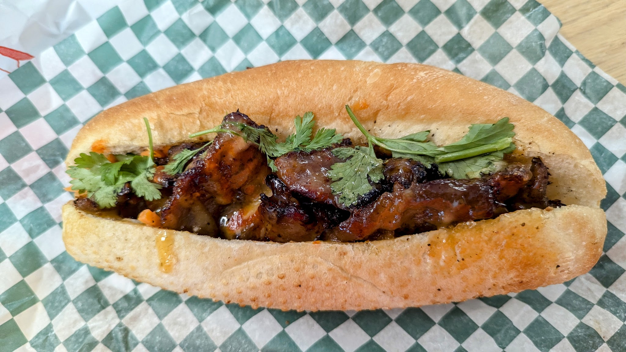 Charbroiled pork banh mi sandwich with cilantro on checkered paper