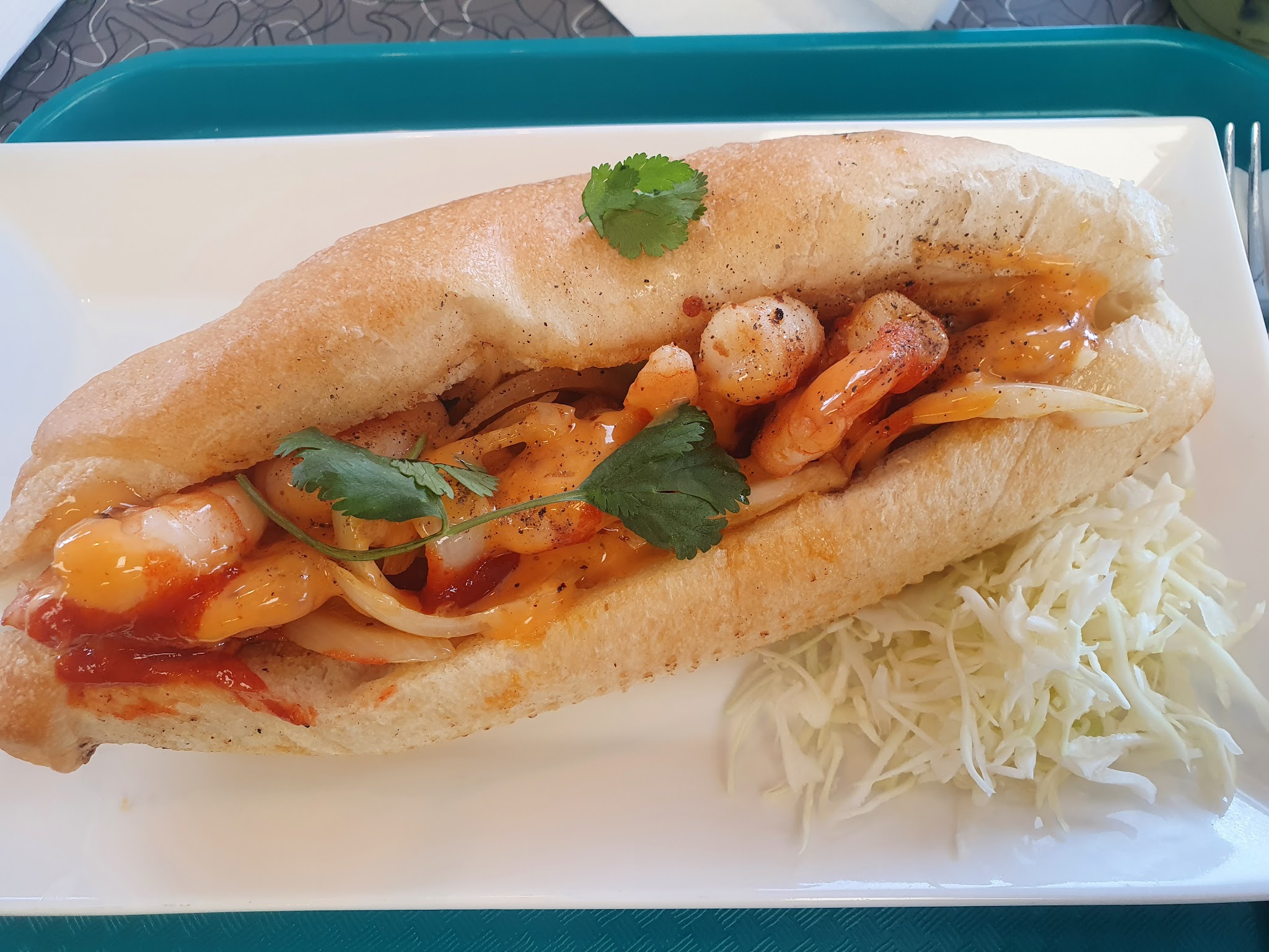 Shrimp banh mi sandwich with sriracha and cilantro on a white plate with coleslaw